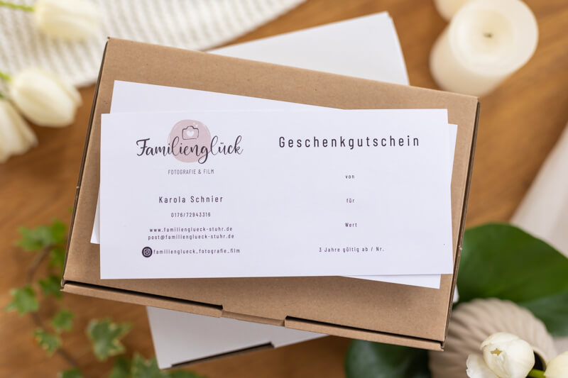 Das Bild zeigt einen Gutschein für ein Familienshooting bei Familienglück Fotografie und Film, der liebevoll als Flatlay arrangiert wurde.