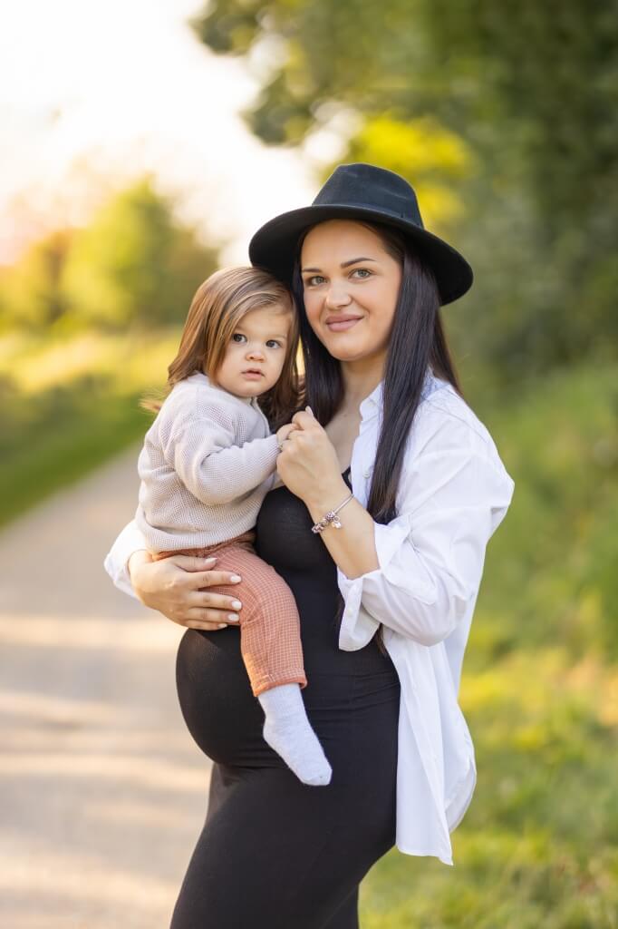 Eine schwangere Frau mit schwarzem Kleid und weißer Bluse hält ihren Sohn bei einem Babybauchshooting auf dem Arm und ziert damit einen Teil meiner Galerie.