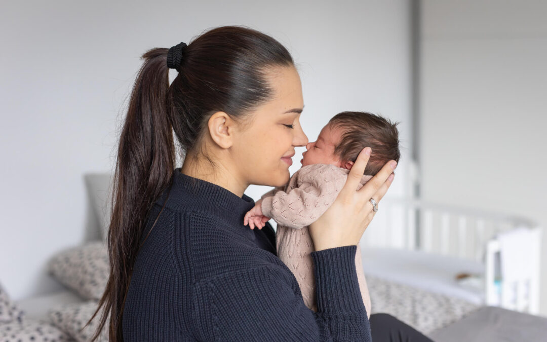 Babyfotoshooting Zuhause: dieses Bild zeigt eine kuschelnde Mama mit ihrem Neugebornen in ihrem Schlafzimmer, Nase an Nase und sehr verliebt.