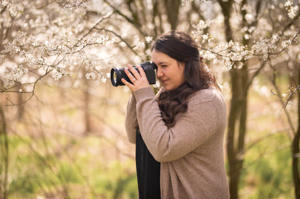 Hier sieht man die Familienfotografin Karola Schnier, während sie bei einem Outdoorshooting ihre Kamera hält und gerade selbst fotografiert für ihren Blog.